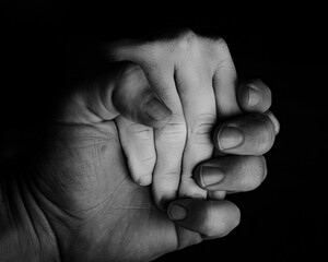 Closeup grayscale shot of holding hands against a black background.