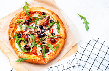 Pizza with salami sausage, mozzarella cheese, mushrooms, black olives, spicy tomato sauce and arugula, white table background, top view