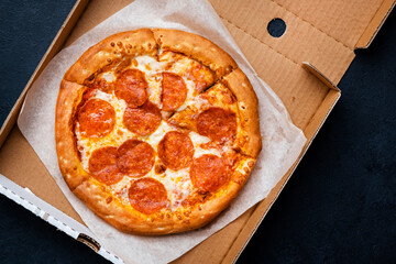 Pepperoni pizza in box with spicy salami sausage, mozzarella cheese, tomato sauce, just delivered,, black table background, top view