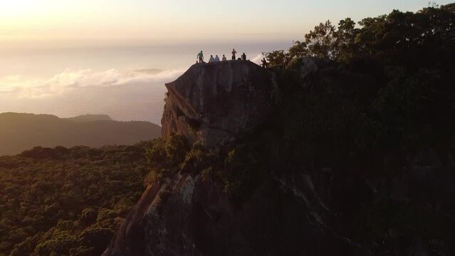 Aerial video of the group of people on the mountain peak surrounded by forest during sunset