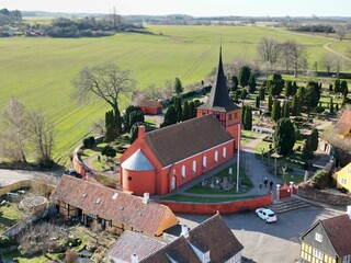 this is an aerial view of a small red church and surrounding green fields