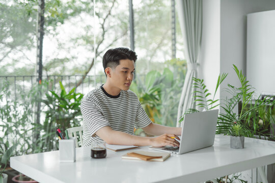 Young handsome minded man sitting at the table and typing a letter