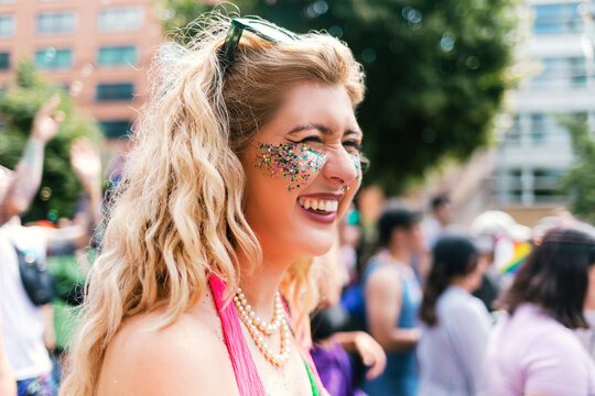 Curly blond Woman with glitter on her face at Pride laughing