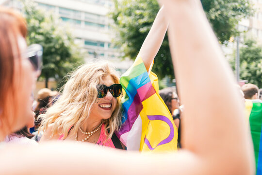 Curly blond Woman with glitter and progress flag at Pride smiling