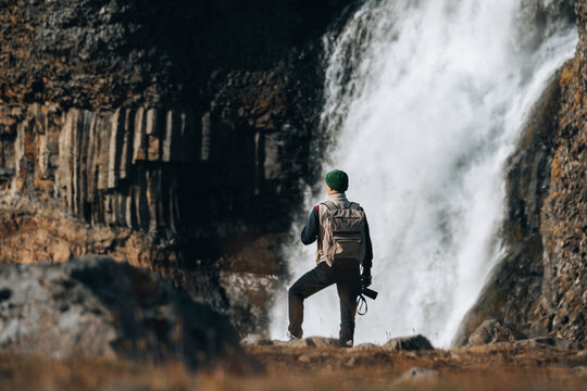 Traveler Man backpacker holds camera taking waterfall landscape photo