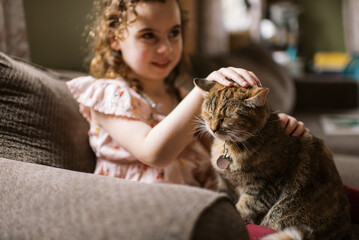 little girl at home on couch petting her pet cat