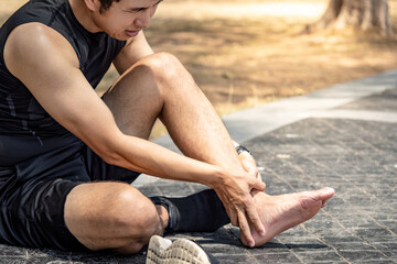 Asian athlete man touching foot in pain due to sprained ankle while running in the park. Broken...