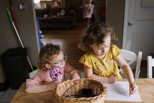 Little girl in yellow shirt drawing a picture at the kitchen table