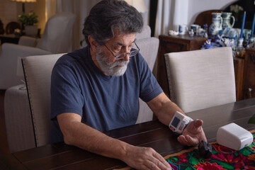 Retired latin man checking his blood pressure at home