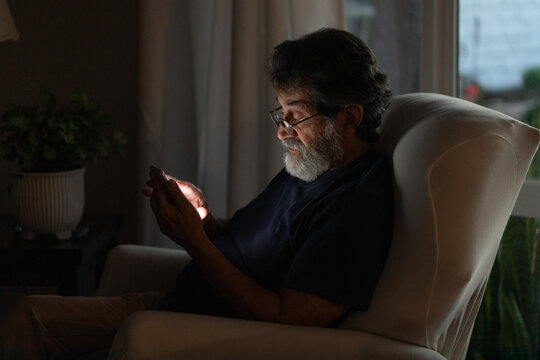 Mature latin man in dark room looking at his phone