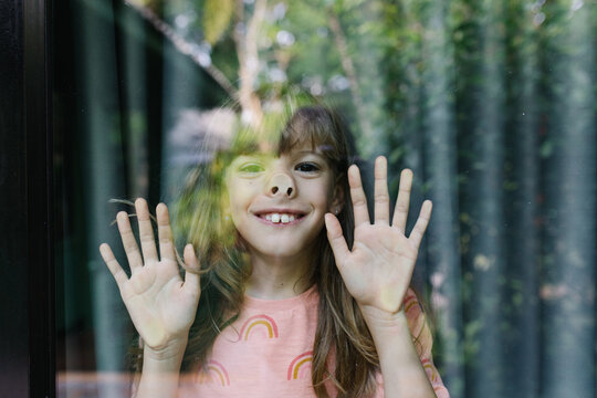 A smiling happy girl looking through the window glass