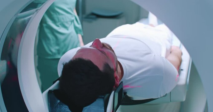 Close-up back shoot of male patient undergoing tomography examination. Man is going into MRI machine. Doctor is performing procedure. Patient is moving at scanner bed. Tomography under infrared rays.