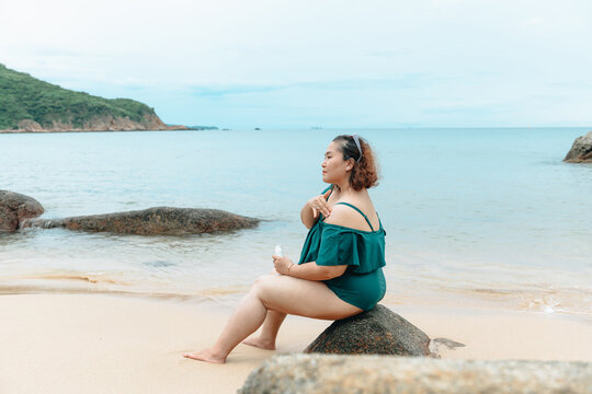 Curvy woman rubs sunscreen on her shoulder.