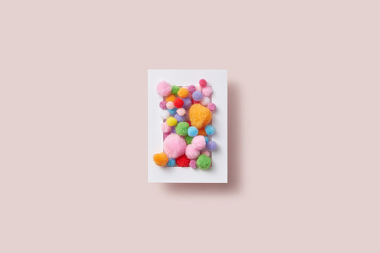 Colorful fluffy pompons in white paper frame.