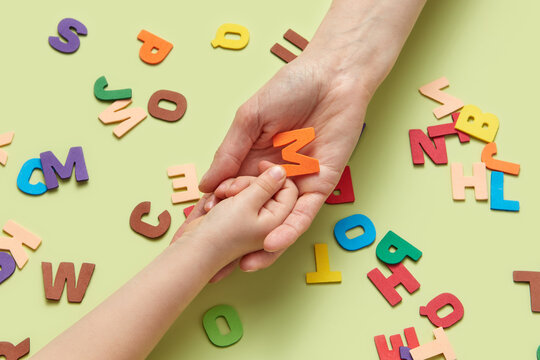 Paper letter M being given from child to mother's hand.
