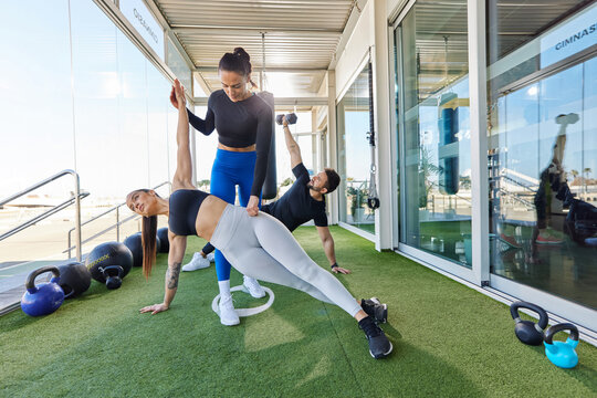 Trainer helping sportspeople doing plank in gym - Powered by Adobe