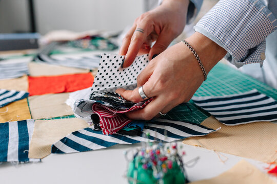 Crop female patchwork artist selecting pieces of cloth in atelier. 