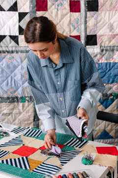 Young female patchwork artist selecting pieces of cloth in atelier. 