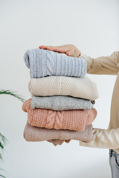 Crop female holding stack of various sweaters 