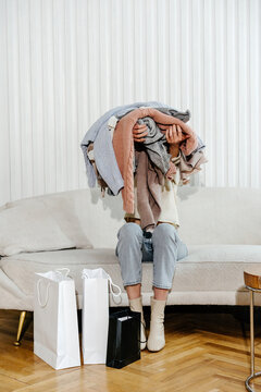 Anonymous sitting on couch covering face with pile of clothes in arms 