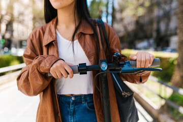 Crop stylish woman with electric scooter in city