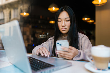 Focused Asian woman working on laptop in cafe