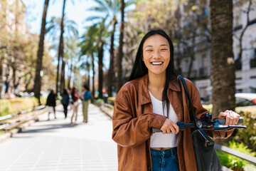 Cheerful Asian woman with electric scooter on walkway