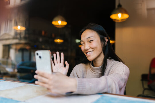 Delighted Asian woman greeting friend during video call