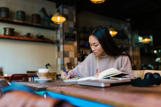 Pensive Asian woman taking notes during studies in cafe