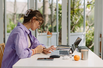 Woman with laptop checking time at home office