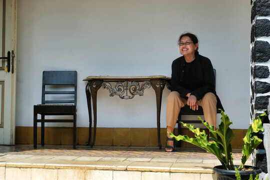 A middle-aged woman in black shirt is sitting on a wooden chair; happy expression