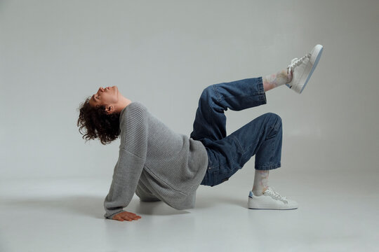 Young man in stylish outfit dancing in gray studio