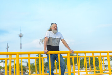 Long-haired, gray-haired man on a pedestrian bridge overlooking the city.