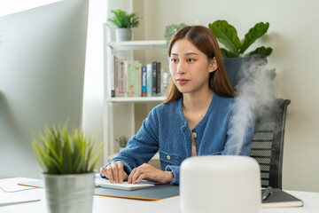 Modern air humidifier device during sitting workplace, happy asian young woman using computer work...