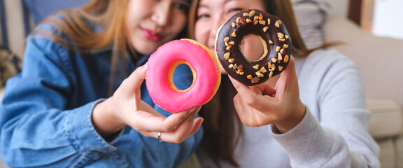 Closeup image of a young couple women holding and showing a piece of donut together