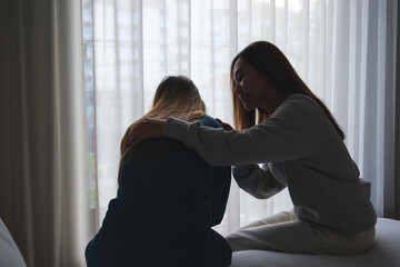 Silhouette image of a woman touching her friend shoulder to comforting and giving encouragement in bedroom