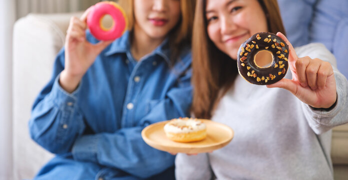Closeup image of a young couple women holding and showing a piece of donut together