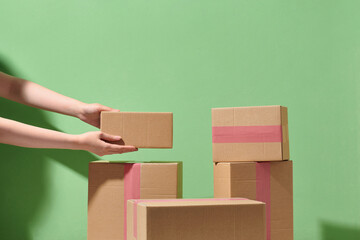 Woman's hands holding boxes stacked on pale pink background.
