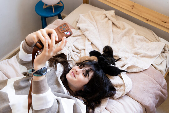 Preteen girl taking a selfie with phone with newborn Kittens at bed 