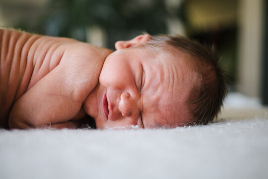 Wrinkly squinting newborn on blanket.