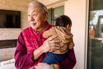 Happy and smiling asian grandfather holding his baby grandson 