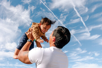 Loving father holding his infant son up high against the sky