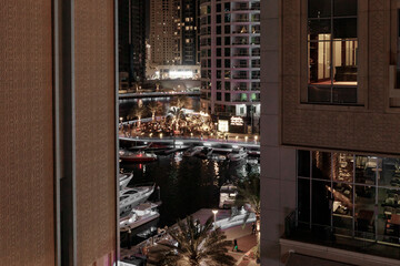 Night view from the promenade of Dubai Marina with illuminated skyscrapers, a water channel, yachts and ships in Dubai city, United Arab Emirates