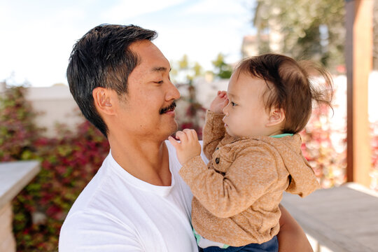 smiling asian father holding baby boy in his arms outdoors on patio