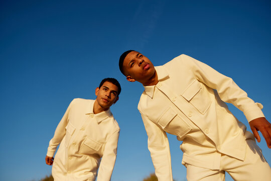 Male friends in white trendy clothes against blue sky