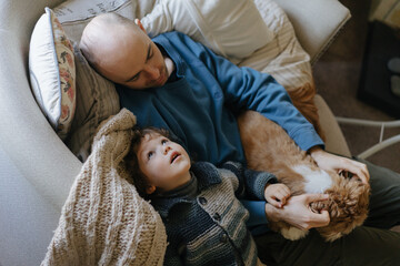 Father and son resting on the couch with dog