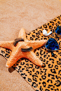 fake eylashes, starfish and sunglasses on a beach towel