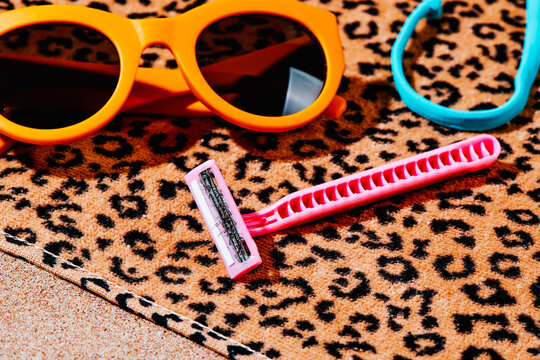 used pink razor and sunglasses on a beach towel
