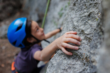 rock climber's hand close-up. child rock climber in a blue protective helmet overcomes the route in the mountains. children's sports in nature.