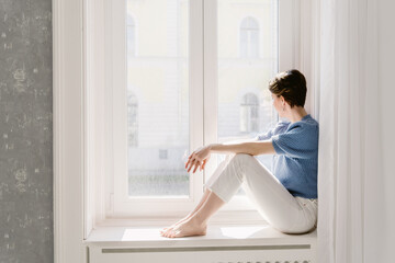 Young woman sitting in a window looking out. 